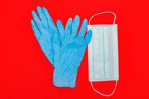 paire de gants médicaux en latex bleu et masque chirurgical à boucle d'oreille sur fond rouge. concept de protection contre les coronavirus. photo