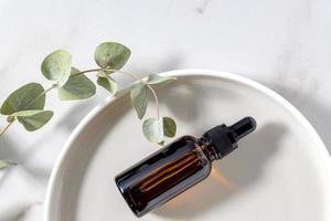 bouteille en verre ambré avec feuilles d'eucalyptus sur plateau rond en céramique. huile essentielle visage et corps pour les soins de la peau photo