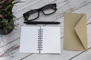 bloc-notes avec enveloppe brune, lunettes de lecture, stylo et plante en pot sur un bureau en bois photo
