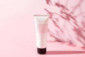 tube cosmétique blanc sur un fond pinl avec des ombres de feuilles. crème nourrissante et hydratante pour le visage, crème pour les mains ou lotion spf. tube cosmétique pour femmes avec un produit de soin de la peau. cosmétiques bio, maquette photo