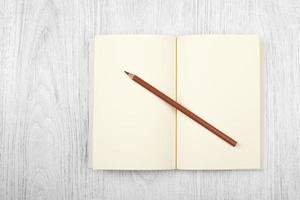 cahier marron ouvert et un crayon sur une table en bois blanc, vue de dessus photo