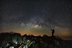 un homme se tient à côté de la galaxie de la voie lactée pointant sur une étoile brillante à doi luang chiang dao avec des signes de point supérieur en langue thaïlandaise. photographie longue exposition.avec grain photo