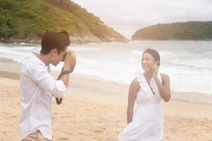 heureux jeune couple vêtu d'une robe blanche aime prendre des photos sur la plage en vacances, voyage, romantique, concept de mariage