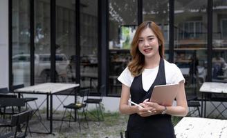 portrait, belle serveuse asiatique millénaire ou propriétaire de restaurant debout devant l'entrée de son restaurant. concept de propriétaire d'entreprise de restaurant ou de café. photo