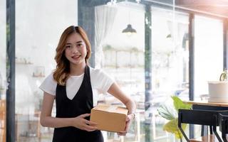 portrait d'une jeune femme asiatique sme travaillant avec une boîte à la maison le lieu de travail. propriétaire de petite entreprise de démarrage, entrepreneur de petite entreprise sme ou entreprise indépendante en ligne et concept de livraison. photo