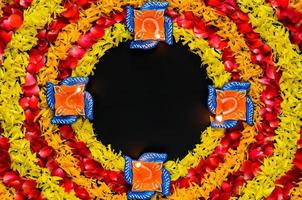 souci décoratif et pétales de fleurs de rose rangoli pour le festival de diwali avec des lampes diya en argile allumées avec une flamme de mise au point floue sur fond noir. photo