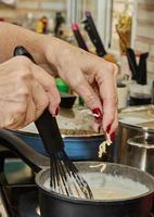 le chef jette du fromage râpé dans une casserole de sauce béchamel, qui est cuite sur une cuisinière à gaz photo