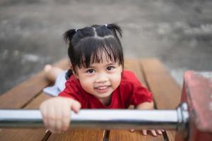 jolie fille asiatique joue dans la cour ou l'aire de jeux de l'école ou de la maternelle. activité estivale saine pour les enfants. petite fille asiatique grimpant à l'extérieur sur l'aire de jeux. enfant jouant sur une aire de jeux extérieure. photo