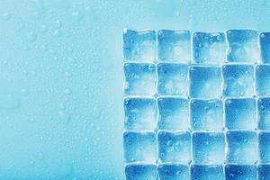 cubes de glace avec des gouttes d'eau éparpillées sur un fond bleu, vue de dessus. photo