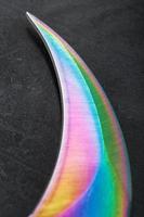 la lame tranchante du couteau kerambit en acier est multicolore en gros plan sur un fond sombre. photo