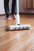 un aspirateur sans fil nettoie le parquet du salon avec le bas des jambes. photo