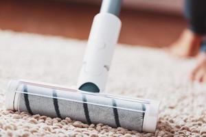 les jambes humaines et une brosse turbo blanche d'un aspirateur sans fil nettoient le tapis de la maison photo