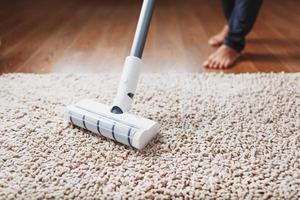 les jambes humaines et une brosse turbo blanche d'un aspirateur sans fil nettoient le tapis de la maison photo