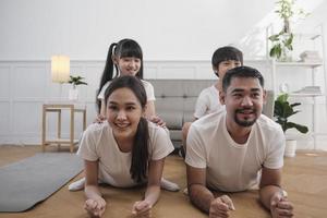 heureux bien-être famille thaïlandaise asiatique, les enfants jouent et taquinent leurs parents pendant l'entraînement de yoga et l'exercice de santé ensemble dans le salon blanc, le mode de vie domestique, l'activité du week-end. photo