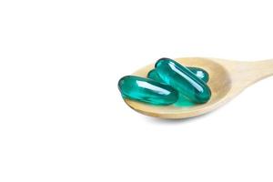 Capsules molles bleu aqua sur cuillère en bois isolées sur fond blanc. Le fichier contient un chemin de détourage. photo