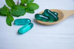 capsules bleues dans une cuillère en bois avec des feuilles de menthe sur fond de bois blanc. photo