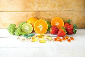 multivitamines et suppléments avec des fruits frais et sains sur fond de bois blanc. photo