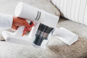 la main d'un homme tient un aspirateur sans fil moderne pour nettoyer le canapé de la maison. photo