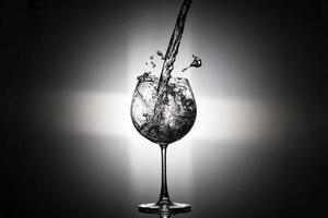 verser de l'eau dans le verre à vin avec feu arrière sur fond noir photo