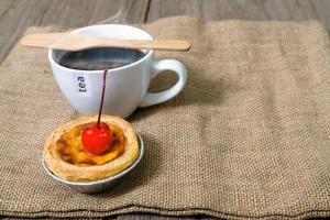 tarte aux oeufs dans une tasse de papier d'aluminium avec cerise rouge et café sur table en bois photo