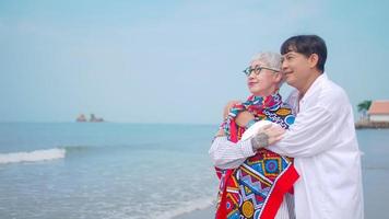 couple de retraités asiatiques se relaxant au bord de la mer en été. un homme âgé prenant soin de son partenaire en se tenant debout sur la plage. photo