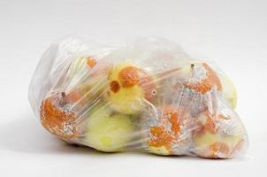 sac en plastique avec des pommes pourries gâtées sur fond blanc. photo