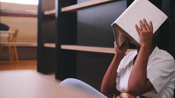 une écolière s'ennuie à lire des livres tout en se préparant aux examens tout en étant assise à la bibliothèque. photo