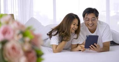 heureux couple asiatique regardant une tablette ensemble dans une chambre. photo