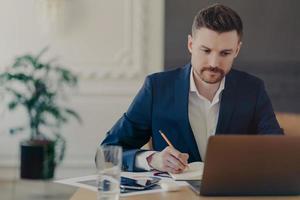 jeune beau directeur exécutif travaillant devant un ordinateur portable au bureau à domicile photo