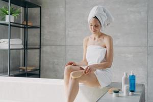 massage anticellulite à la brosse sèche. jolie femme caucasienne enveloppée dans une serviette après le bain. photo