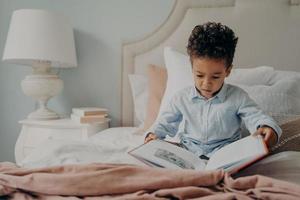mignon petit garçon afro-américain essayant de lire un livre pour enfants photo