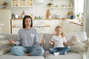 mère, fille adoptive pratiquent le yoga assis sur un canapé à la maison. mode de vie sain, adoption d'un enfant photo