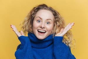 le modèle féminin assez étonné et ravi exprime la positivité, a une expression heureuse, fait des gestes actifs, voit quelque chose d'inattendu et de surprenant, isolé sur fond jaune. couleurs vives photo