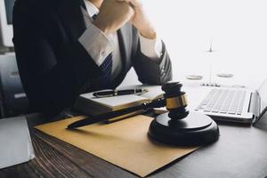 concept de justice et de droit. juge masculin dans une salle d'audience avec le marteau, travaillant avec, clavier d'ordinateur et d'accueil, lunettes, sur table à la lumière du matin photo