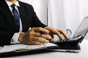 concept de comptabilité d'entreprise, homme d'affaires utilisant une calculatrice avec ordinateur portable, budget et papier de prêt au bureau. photo