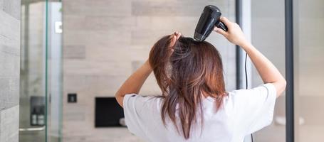 jeune femme utilisant un sèche-cheveux à la maison ou à l'hôtel. coiffures et concepts de style de vie photo
