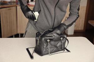 voleur en tenue noire et gants voir dans le sac ouvert des femmes volées. le voleur sort l'or et l'argent d'un sac à main de femme dans la cuisine photo