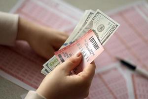 une jeune femme tient le billet de loterie avec une rangée complète de chiffres et de billets d'un dollar sur l'arrière-plan des feuilles vierges de loterie photo