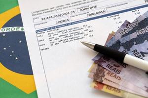 rapport de preuve de collecte brésilien avec des factures d'argent en réaux brésiliens et un stylo sur fond de drapeau national. paiement légal des impôts brésiliens et déclaration fiscale photo