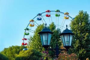 paysage d'un parc d'attractions avec lanterne décorée de fleurs en arrière-plan le sommet d'une grande roue montrant au-dessus de la cime des arbres contre un ciel. photo