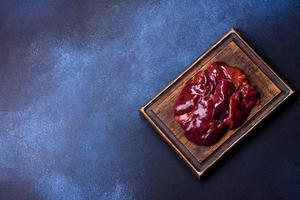 morceaux de foie cru sur une planche à découper en bois sur un fond de béton foncé photo