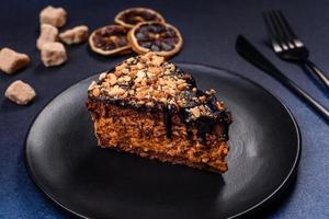 un morceau de délicieux gâteau frais aux noix et au chocolat sur une plaque noire sur fond bleu foncé photo