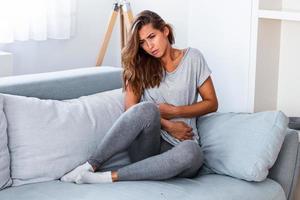 femme dans une expression douloureuse se tenant la main contre le ventre souffrant de douleurs menstruelles, allongée triste sur son lit à la maison, ayant une crampe abdominale dans le concept de santé féminine photo