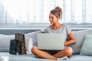 jeune femme tenant une carte de crédit et utilisant un ordinateur portable. concept de magasinage en ligne. femme heureuse faisant des achats en ligne à la maison photo