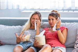 des filles tristes regardent un film en pleurant pour un film touchant. deux meilleurs amis regardent un film triste à la maison au lit en pleurant de toucher.