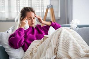 femme malade avec des maux de tête assis sous la couverture. femme malade avec des infections saisonnières, grippe, allergie au lit. femme malade recouverte d'une couverture allongée dans son lit avec une forte fièvre et une grippe, se reposant. photo