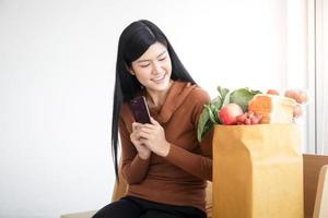 belle femme asiatique souriante tenant un smartphone pour commander de la nourriture en ligne. le concept commercial des services de livraison de nourriture pendant le coronavirus. copie espace photo