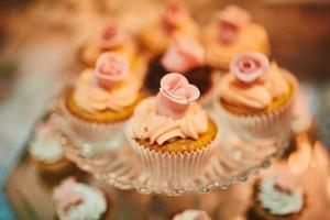 muffin festif à la crème vive sur support en verre. cupcake décoré de décor rose et crème, mini gâteau, pâtisseries sur fond bois. barre de biscuits. photo de haute qualité. mise au point sélective