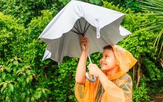 un garçon asiatique met un imperméable et ouvre un parapluie un jour de pluie. photo