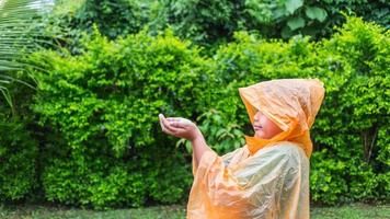 un garçon asiatique portant un imperméable orange est heureux et s'amuse sous la pluie un jour de pluie. photo